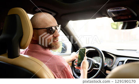 Man driving a car while holding a smartphone and wearing sunglasses 129190170