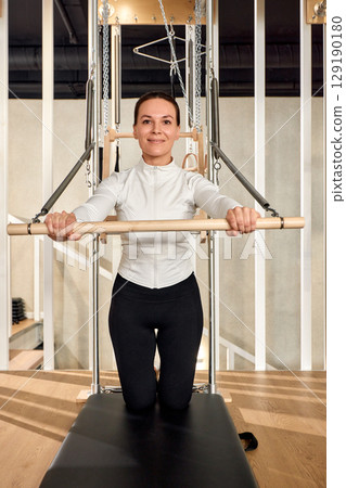Woman practicing pilates on equipment in a modern fitness studio Woman practicing pilates on equipment in a modern fitness studio 129190180