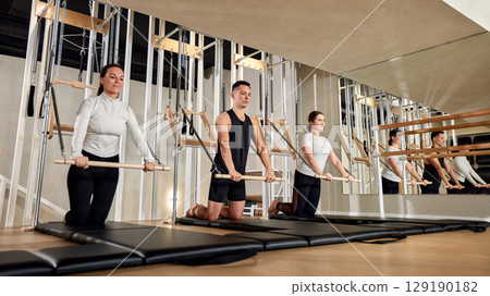 Group of individuals performing pilates exercises in a modern fitness studio Group of individuals performing pilates exercises in a modern fitness studio 129190182