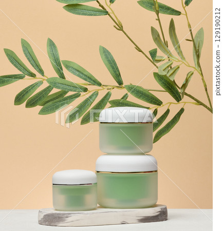 Green plastic jars with cream on beige background, cosmetics Green plastic jars with cream on beige background, cosmetics 129190212