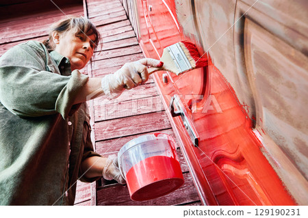 Flat brush used by professional painter for application of metal paint on entrance metal door of rural house, scene shows painting in progress. 129190231