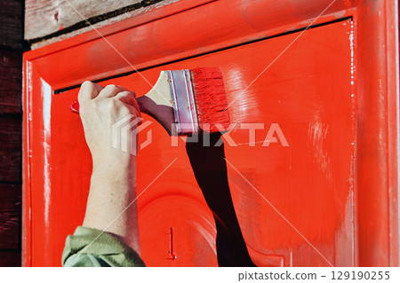 Flat paint brush applies rust resistant paint to metal door, ensuring protection for country house entrance. Flat paint brush applies rust resistant paint to metal door, ensuring protection for country house entrance. 129190255