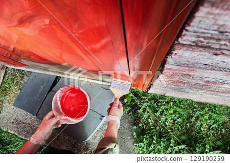 House painter applies red paint to metal door using flat brush. House painter applies red paint to metal door using flat brush. 129190259
