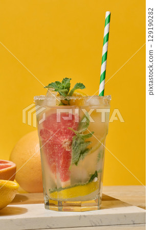 Glass with cool drink garnished with mint, lemon and grapefruit. White marble coaster background Glass with cool drink garnished with mint, lemon and grapefruit. White marble coaster background 129190282