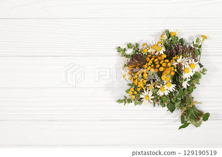 Floral arrangement of wild herbs and flowers on a wooden table, rustic style, Bouquet of tansy, mint, celandine, chamomile and yarrow, collection of useful herbs for treatment according 129190519