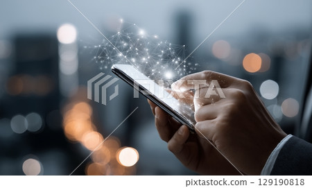 Businessman navigating smartphone, glowing network hologram projecting from screen against blurred nighttime cityscape, representing global digital Professional businessman 129190818