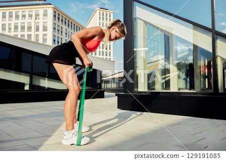 Young woman using a resistance band for a workout on a modern terrace Young woman using a resistance band for a workout on a modern terrace 129191085