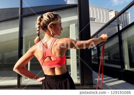 Active Woman Working Out with Resistance Band Outdoors in the Sunlight 129191086