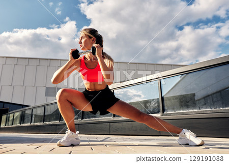 Woman performing fitness exercises with weights outdoors under a bright blue sky 129191088