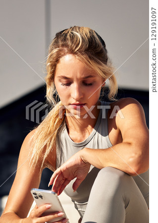 Young woman sitting outdoors focusing on her smartphone in bright sunlight Young woman sitting outdoors focusing on her smartphone in bright sunlight 129191097