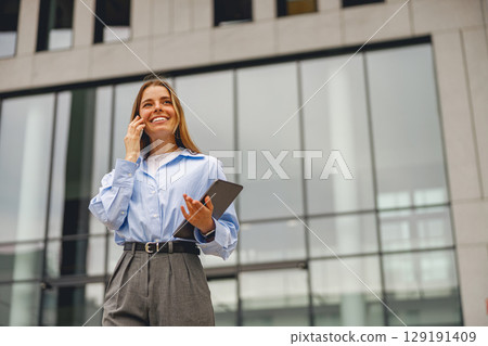 A successful businesswoman engaged in a phone conversation outside a contemporary office building A successful businesswoman engaged in a phone conversation outside a contemporary office building 129191409