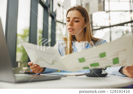 A Young Woman Engaged in Analyzing Business Charts and Data at a Modern Workspace Setting 129191410