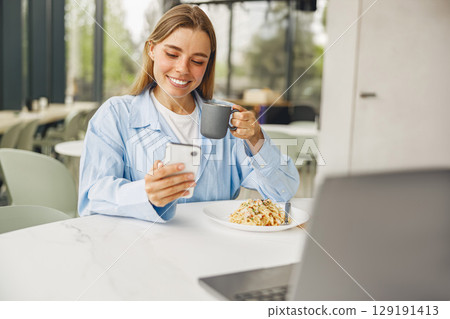 Enjoying a Casual Morning Coffee and Engaging in Phone Interaction in a Modern Cafe Setting 129191413