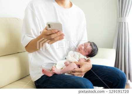 Family: Dad looking at his smartphone while holding a baby Family: Dad looking at his smartphone while holding a baby 129191720