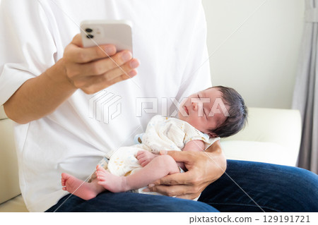 Family: Dad looking at his smartphone while holding a baby 129191721