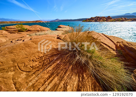 Red Sandstone Heart Carving Desert Bush and Blue Reservoir Eye Level View 129192070
