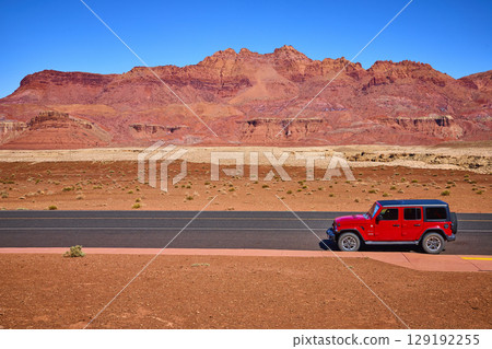 Red SUV on Desert Highway with Red Rock Formations Eye Level Perspective Red SUV on Desert Highway with Red Rock Formations Eye Level Perspective 129192255