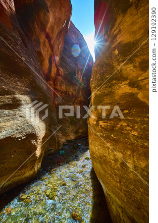 Sunlit Sandstone Walls and Flowing Stream in Kanarra Slot Canyon Low Angle View 129192390