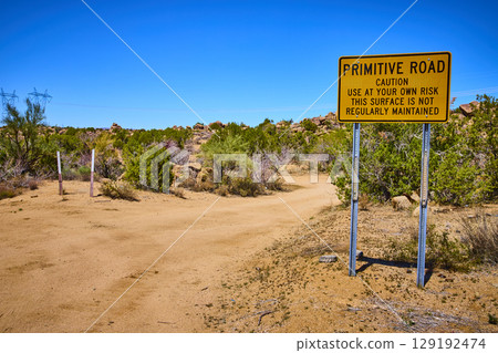 Desert Caution Sign on Primitive Road with Power Lines and Brush Eye Level View 129192474