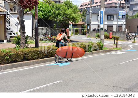 A man on a bicycle returning home after surfing A man on a bicycle returning home after surfing 129194348
