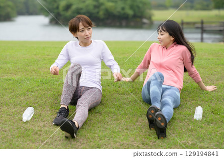 Two women resting on the grass after exercise Two women resting on the grass after exercise 129194841