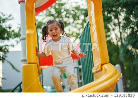 happy toddler baby girl sliding and playing at playground 129195020