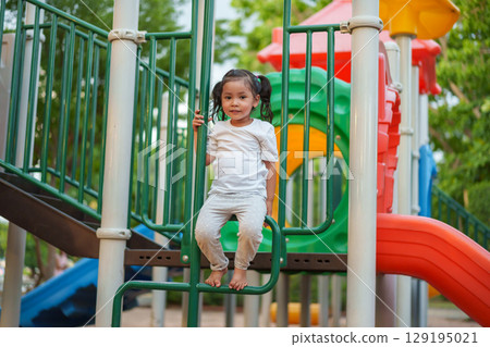 happy toddler girl playing and climbing on outdoor playground at park 129195021