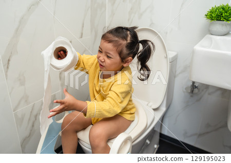 happy toddler girl is sitting on toilet with tissue at home. potty training and learning happy toddler girl is sitting on toilet with tissue at home. potty training and learning 129195023