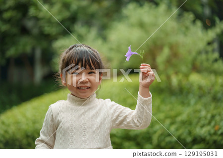 happy toddler girl in white dress with Ruellia simplex or Mexican petunia flower in garden 129195031