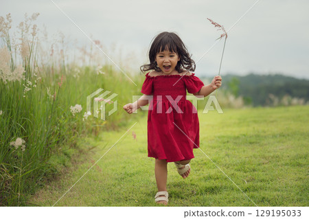 happy toddle girl in red dress running on grass field 129195033