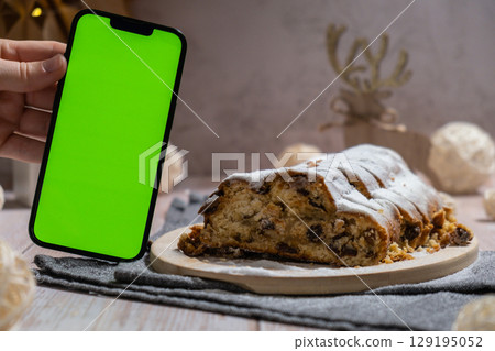 Homemade Christmas traditional cake pie with marzipan nuts and dried fruits pastry dessert stollen. Smartphone with green screen chroma key application website advertisement mock up template. Winter 129195052