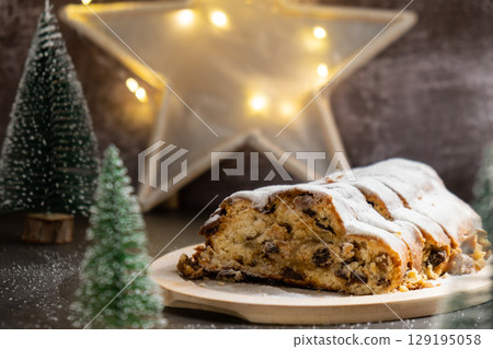Christmas Stollen in Christmas lights and decoration. Traditional sweet fruit loaf with icing sugar festive pastry dessert. Holiday baking food 129195058