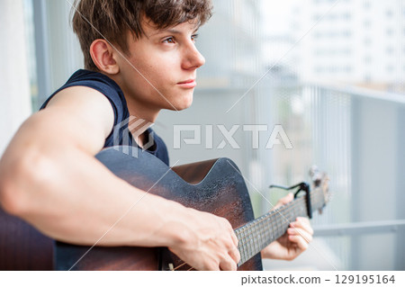 Serious fourteen year old teenage boy calmly playing guitar on balcony Serious fourteen year old teenage boy calmly playing guitar on balcony 129195164