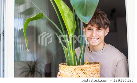 Cute cheerful teenager boy bought and brought home a green houseplant 129195185