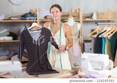 Young dressmaker presenting finished dress to client 129195583