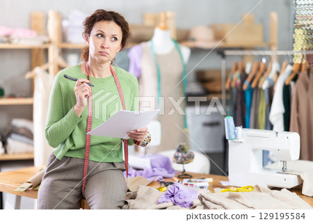 Female seamstress drawing sketches of custom garment by hand in studio 129195584