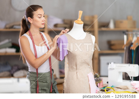 dressmaker works on a dress near a mannequin 129195588