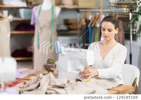 Female seamstress working on sewing machine in workshop Female seamstress working on sewing machine in workshop 129195589