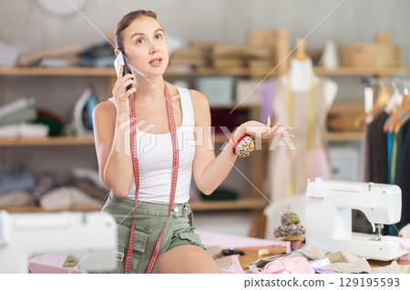 Young seamstress talking on phone in fashion studio 129195593