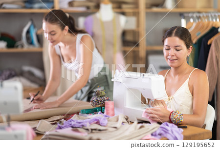 fashion designer draws patterns of dresses next to a seamstress fashion designer draws patterns of dresses next to a seamstress 129195652