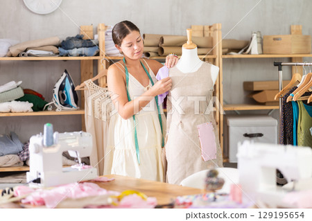 dressmaker works on a dress near a mannequin 129195654
