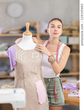 dressmaker works on a dress near a mannequin 129195665