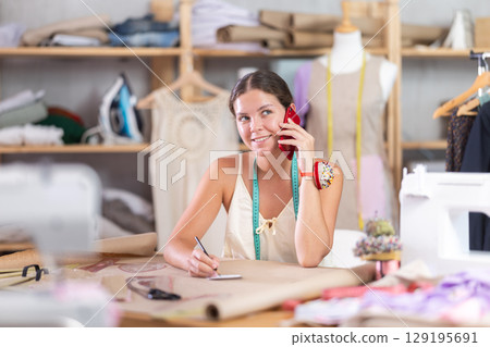Female fashion designer talking on phone in workshop 129195691