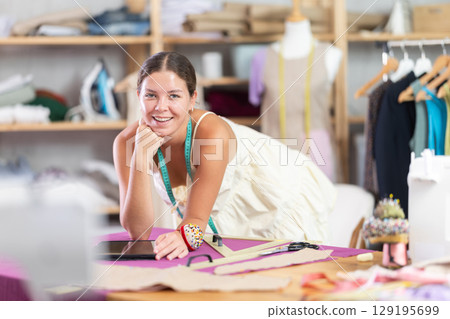 Young female dressmaker drawing on tablet in sewing workshop 129195699