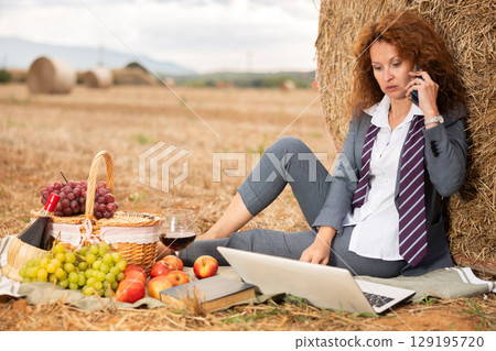Woman in office clothes talking on mobile phone at picnic in field 129195720