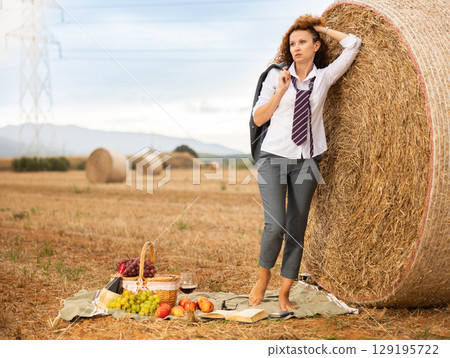 Young woman in white blouse and gray business suit standing on soft plaid mat near stack of straw Young woman in white blouse and gray business suit standing on soft plaid mat near stack of straw 129195722