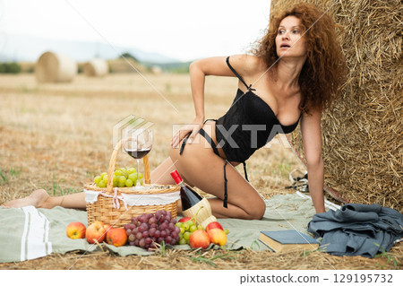 Woman in black lingerie striking erotic pose kneeling near hay bale 129195732