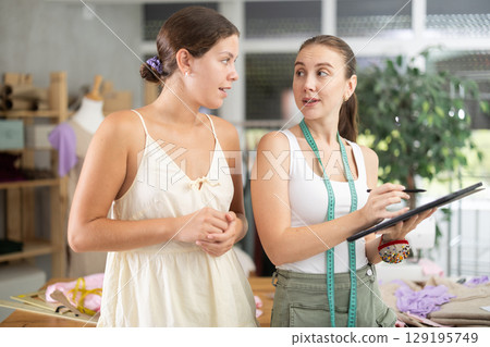 Two female dressmakers drawing a model of clothes on a tablet 129195749