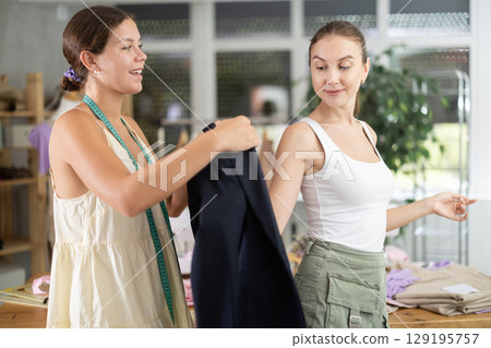 Young tailoress trying ready jacket on female client 129195757