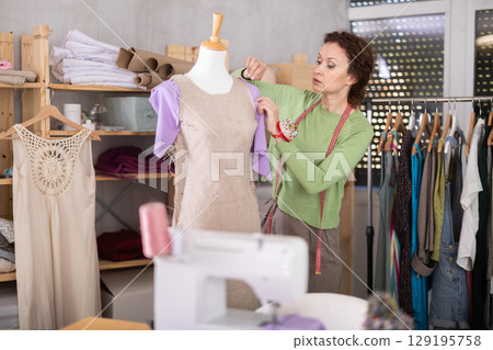 Seamstress shaping dress on mannequin in tailoring studio Seamstress shaping dress on mannequin in tailoring studio 129195758